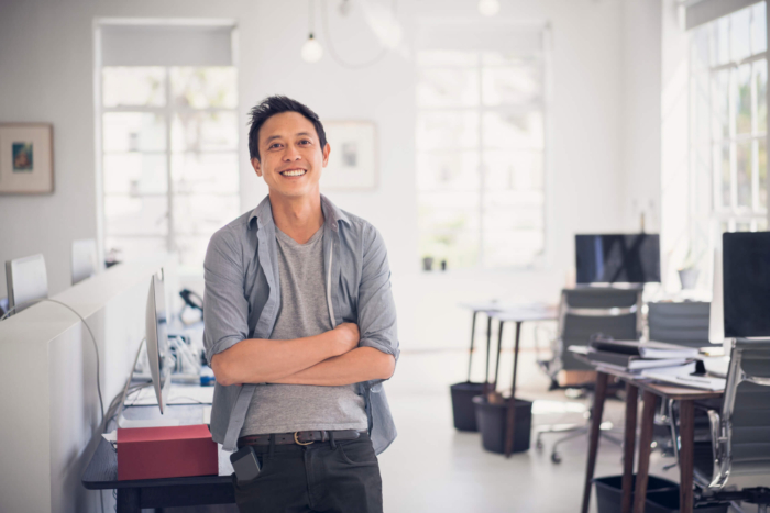 photo of happy businessman leaning on table. Portrait of expert with arms crossed. Smiling professional is in creative office.