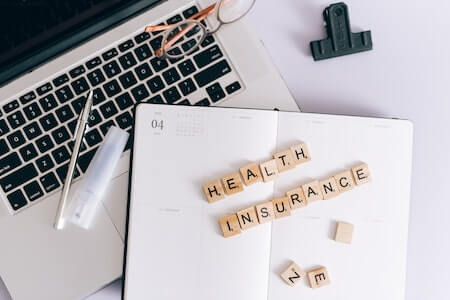 A Health Insurance Spelled on Scrabble Blocks on Top of a Notebook Planner - hiring a part time employee