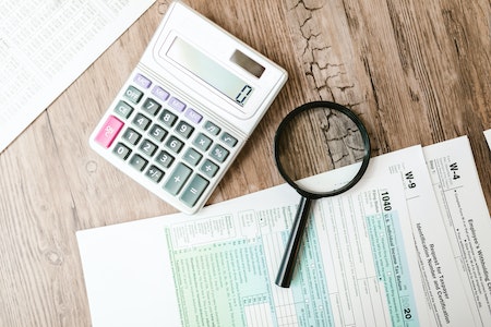 A Calculator and a Magnifying Glass beside Documents - last minute tax filing